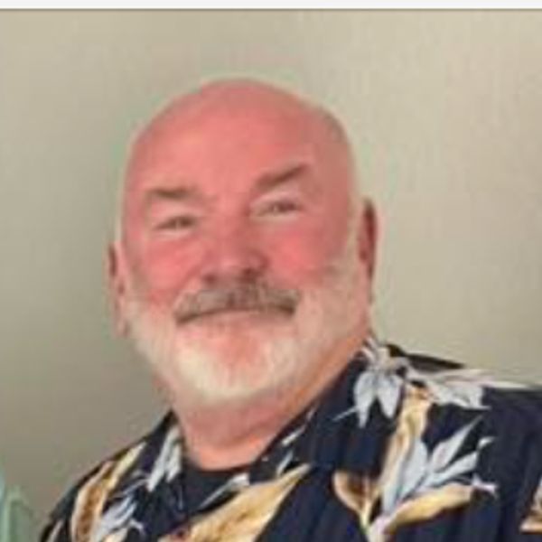 Smiling older man with a white beard in a patterned shirt.