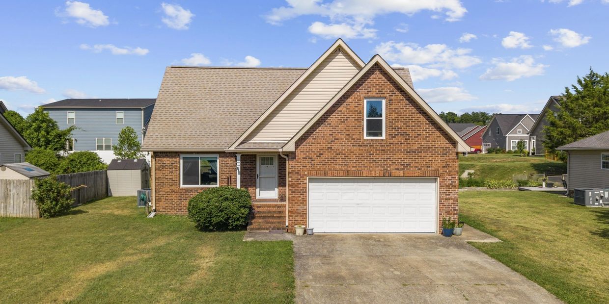 Brick house with a large driveway and lawn under blue sky.