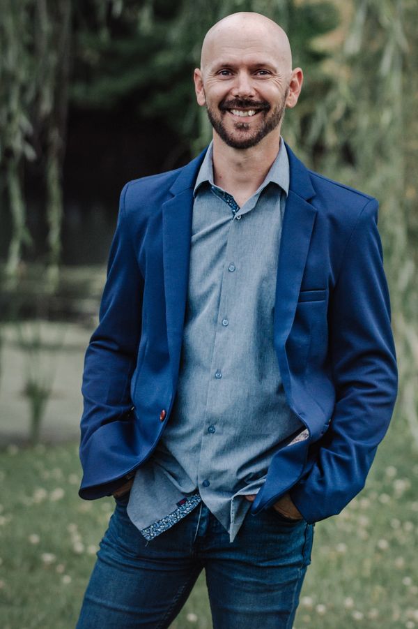 Smiling bald man in blue suit jacket outdoors.