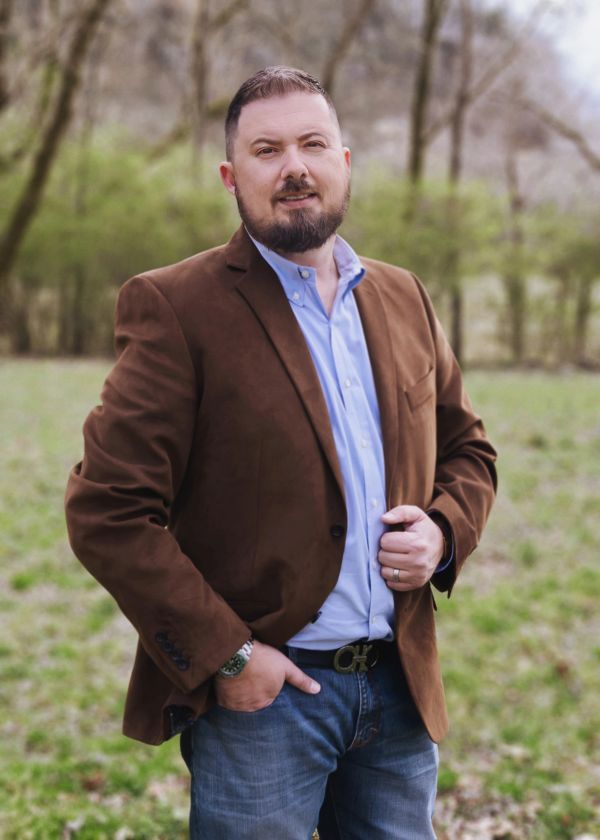 Man in brown blazer posing outdoors.