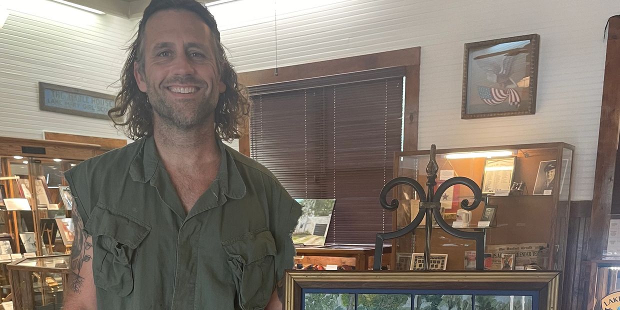 A man standing next to a framed painting on an easel in an art gallery.