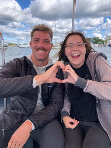 Two friends on a boat making a heart shape with their hands and smiling.