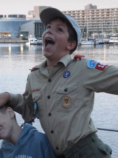 Boy in scout uniform joyfully posing by waterfront with another child.