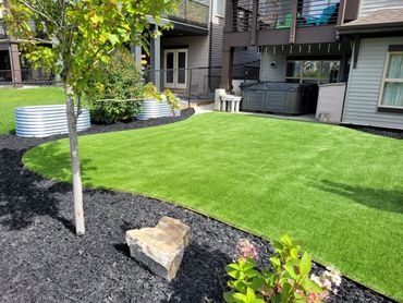 Maintenance free backyard with synthetic grass,black rubber Mulch, planting beds and boulders