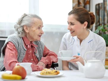 Carer taking care of elderly woman, offering support for breakfast