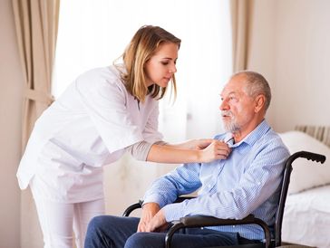 Carer helping elderly man put on a shirt