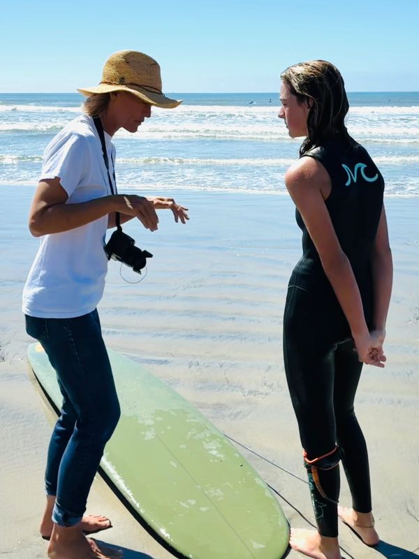 Surf instructor teaching a young surfer on the beach.
