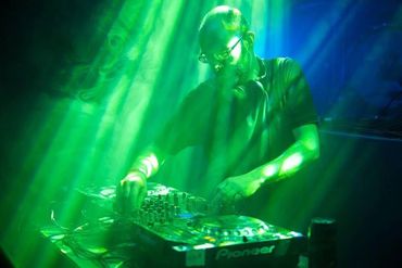 A bearded Dolphin Boy DJ at Edinburgh Cellar Bar & Venue with green lighting cast over him as he pla
