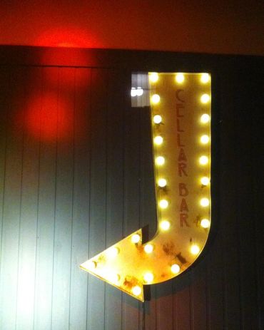 An illuminated arrow sign with Cellar Bar written in red writing, points down and to the left, with