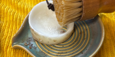 Shaving brush with soap on a ceramic dish.