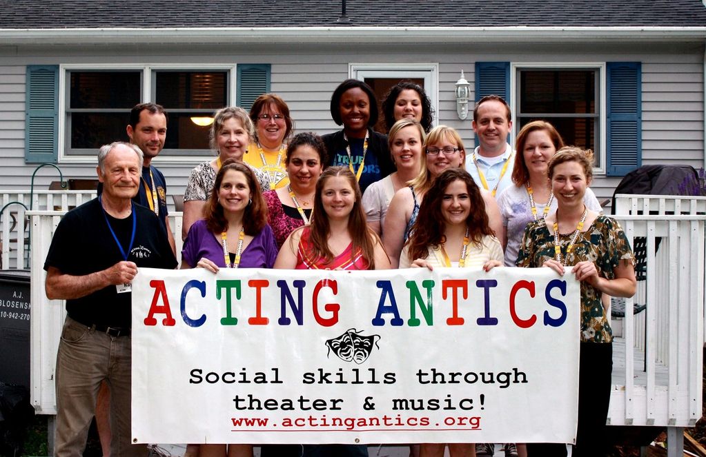 A group of people holding a colorful banner promoting Acting Antics social skills program.