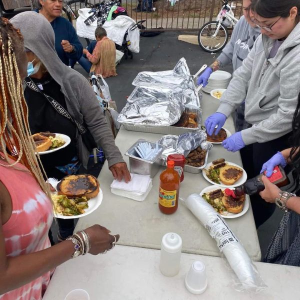 People serving and receiving food at an outdoor event.