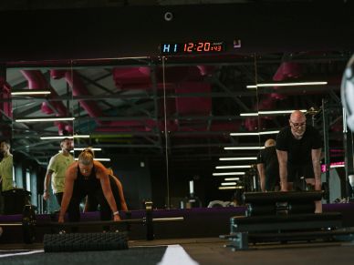 Two people preparing for a workout in a gym with a digital clock above.
