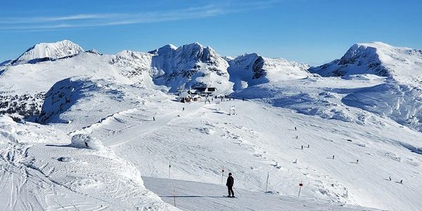 A skier on a snowy mountain slope with clear blue sky.