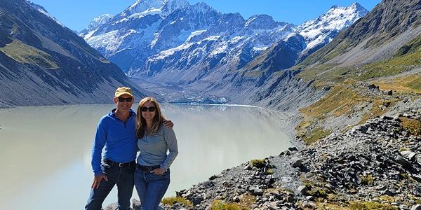 Couple posing by a serene mountain lake with snowy peaks in the background.