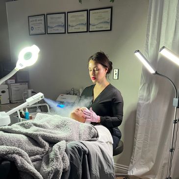 A skincare professional performs a facial treatment in a well-lit room.