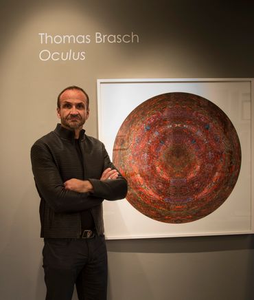 Artist standing in front of red circular symmetrical image in white frame during Oculus show