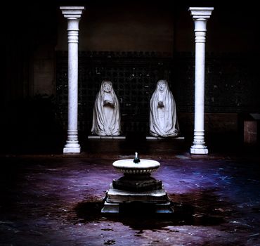 White statues of nuns kneeling in prayer before a Moorish style fountain in a courtyard