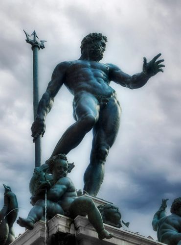 Statue of Neptune with trident against a cloudy sky.  He is holding his trident.