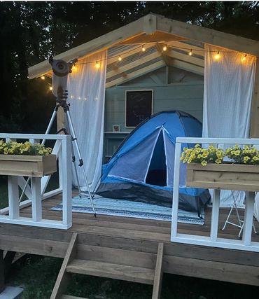 Outdoor playhouse set up with a tent and telescope for a family campout