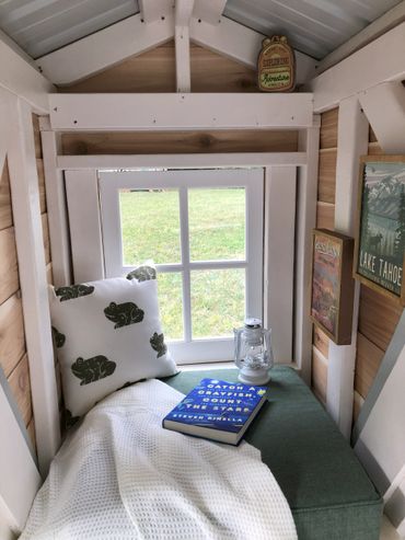 Cozy window seat reading nook inside an a frame playhouse with a pillow, blanket and book