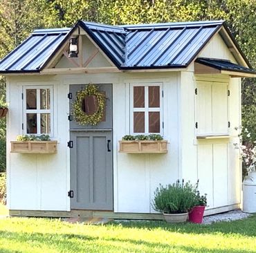 Farmhouse playhouse with white board and batten siding and black metal roof