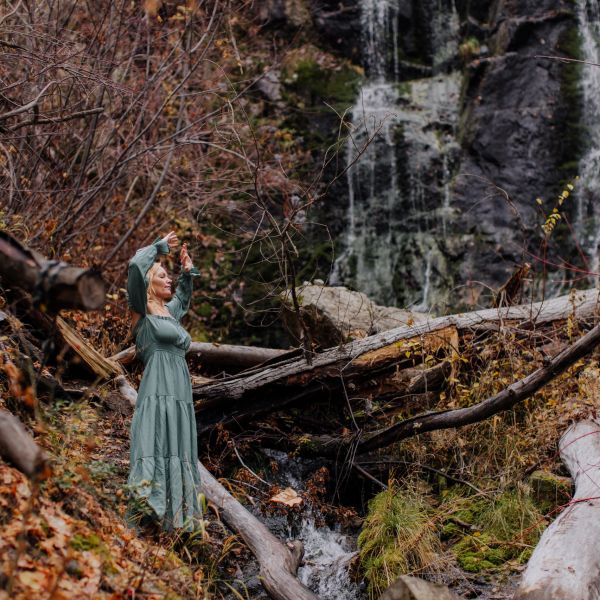 Woman in green dress enjoying nature near a waterfall.