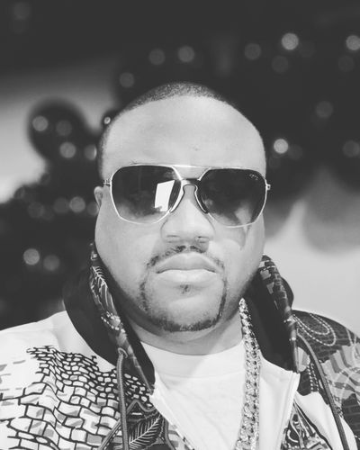 Man wearing sunglasses and a patterned jacket in a black and white photo.