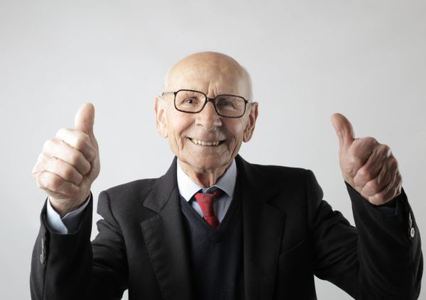 Happy elderly gentleman wearing black suit & tie, giving two thumbs up for great service