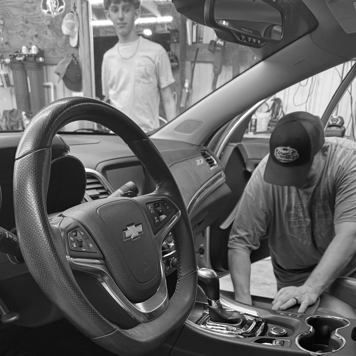 Two men working on a Chevrolet car interior in a garage.