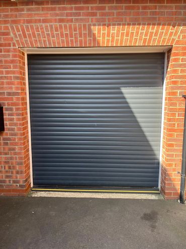 Closed dark gray roller garage door with brick walls.