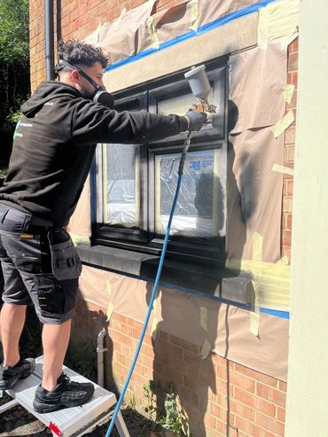 Man spray painting a window frame while wearing protective mask and gloves.