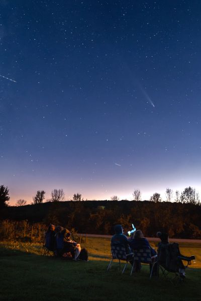 People stargazing on chairs under a clear night sky with a visible comet.