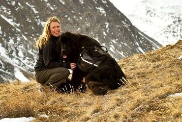 A girl posing in the mountains with a black newfoundland dog