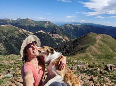 A girl in the mountains with a white and tan border collie