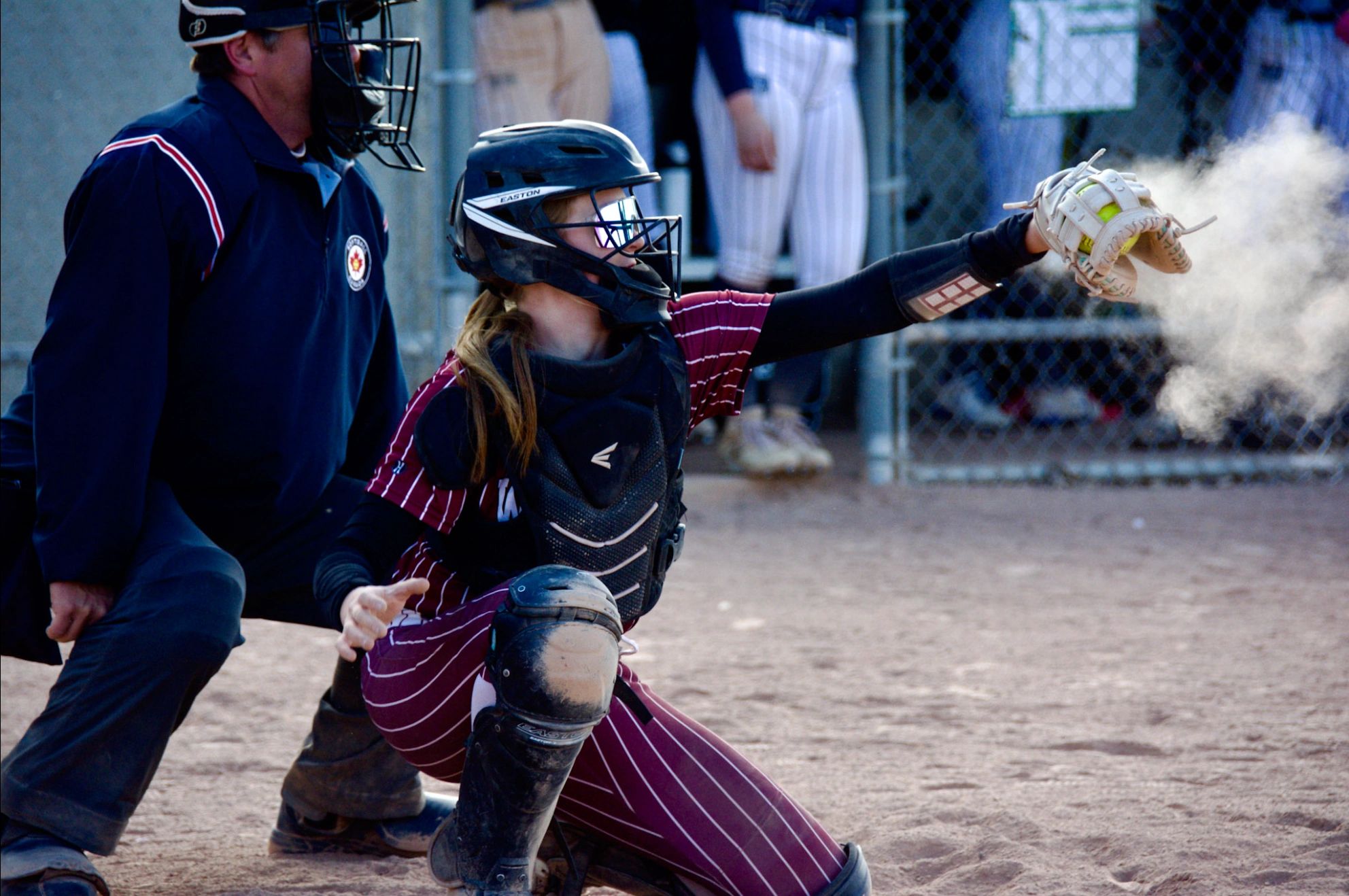 Softball catcher reaching for a ball with an umpire nearby.