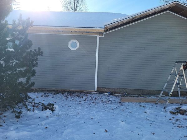 Snow-covered ground with a gray house siding and a ladder beside it.