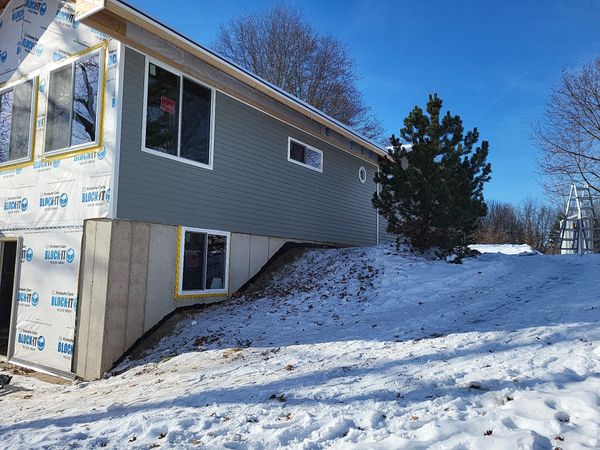 Partially constructed house with snow-covered ground and clear blue sky.