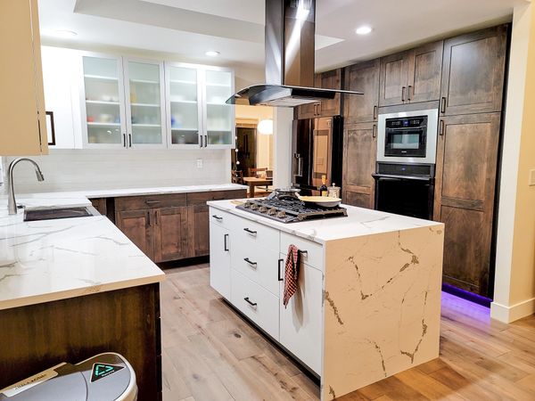 Modern kitchen with marble island and dark wood cabinets.