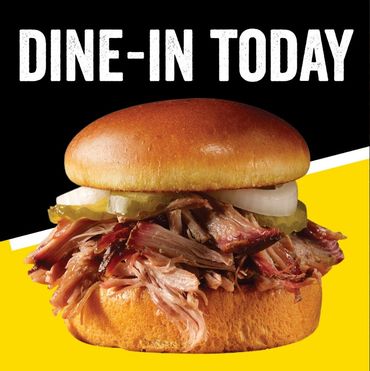 Pulled pork sandwich with onions and pickles, inviting you to dine in today at Dickeys Barbecue.