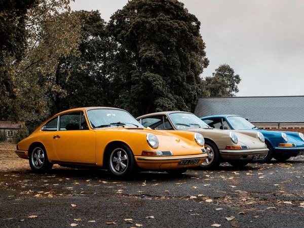 Three vintage Porsche cars parked outdoors on a cloudy day.