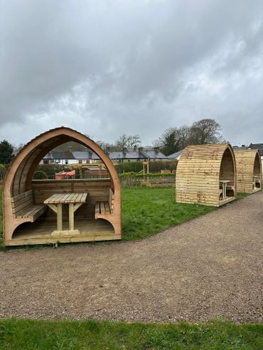 Wooden outdoor seating pods on a cloudy day in a grassy area.