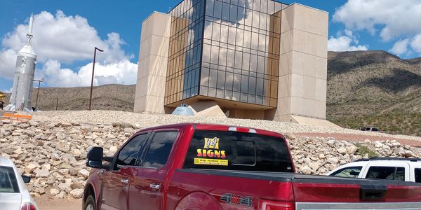 Red pickup truck parked near a modern building in a rocky area.