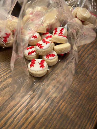 Small baseball-themed cookies in clear plastic bags on a wooden table.