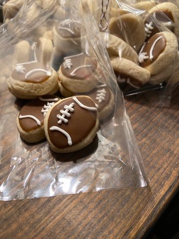 Football-shaped cookies with brown icing and white laces in plastic bags.