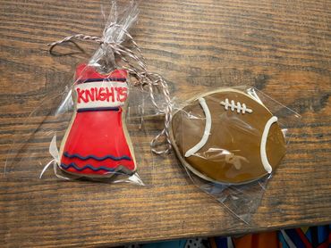 Packaged cookies shaped like a cheerleader dress and a football on a wooden table.