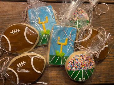 Football-themed decorated cookies wrapped in clear plastic on a wooden surface.