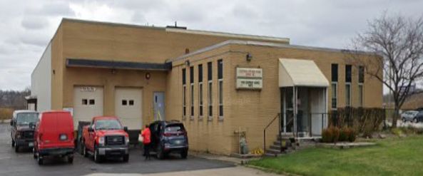 Brick industrial building with parked vehicles and people outside.
