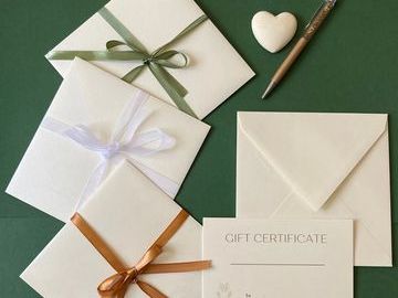 Elegant gift certificates and envelopes with ribbons and a pen on a green surface.