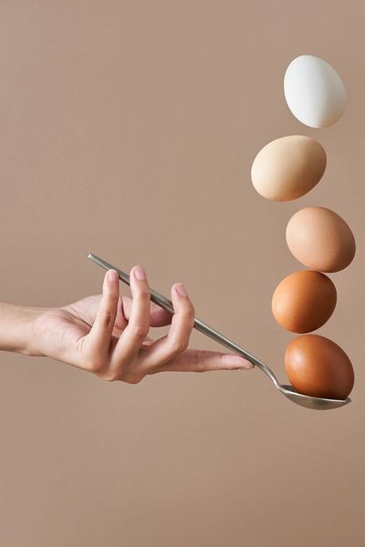 A hand balancing a stack of eggs on a spoon, illustrating egg quality and fertility